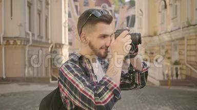 年轻的新手留胡子的摄影师在一个古老城市的街道上拍照，那里有美丽的建筑。 旅游费用